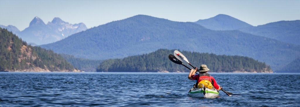 a person in a kayak paddling on the water with mountains in the background