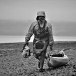 a man walking on the beach carrying a boat