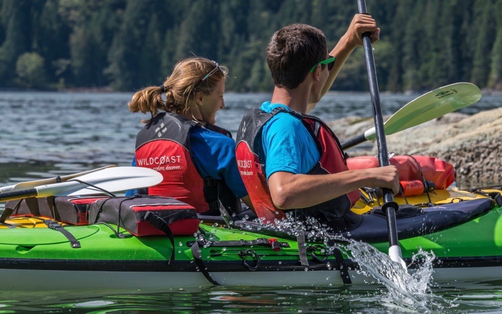 a man and woman are paddling a green kayak