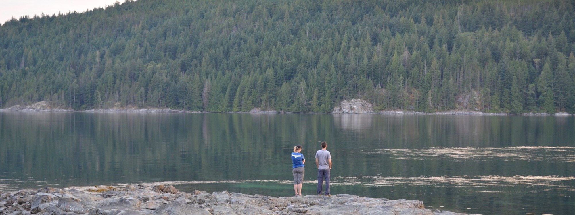 two people standing on rocks near the water