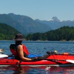 a woman sitting on top of a red kayak in the water