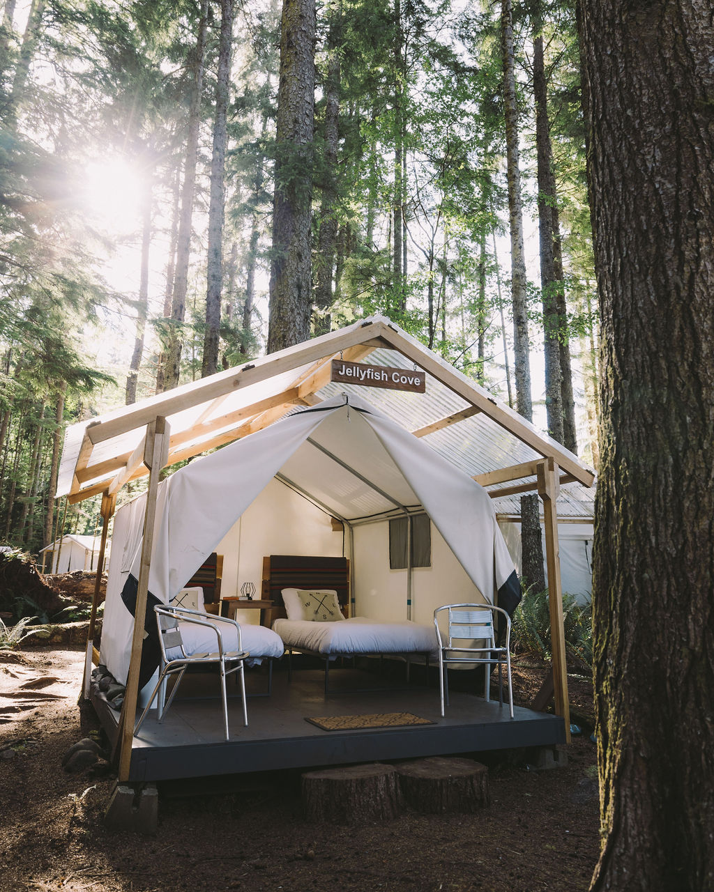 White glamping tent with 2 beds set in green forest.