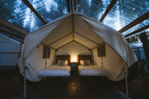 White glamping tent with clear roof, lamp on in tent with multi color blankets