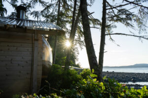 Wooden barrel sauna overlooking the ocean at sunset.
