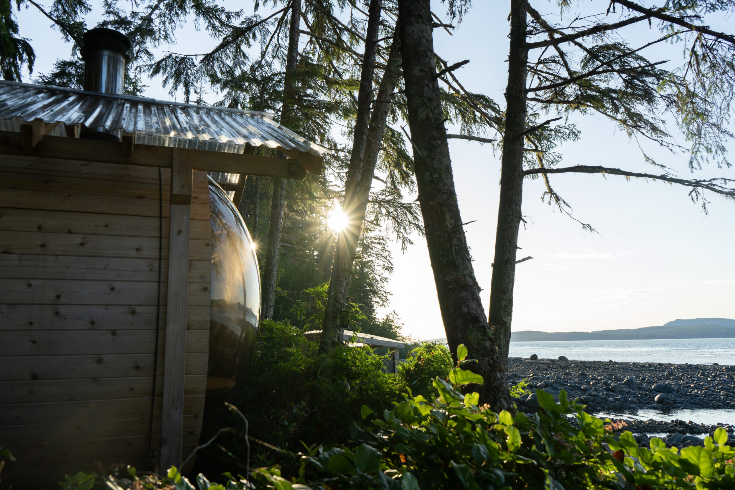 Wooden barrel sauna overlooking the ocean at sunset.