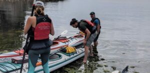 three people standing next to a kayak in the water