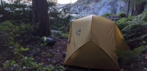 a tent pitched up in the woods next to a river