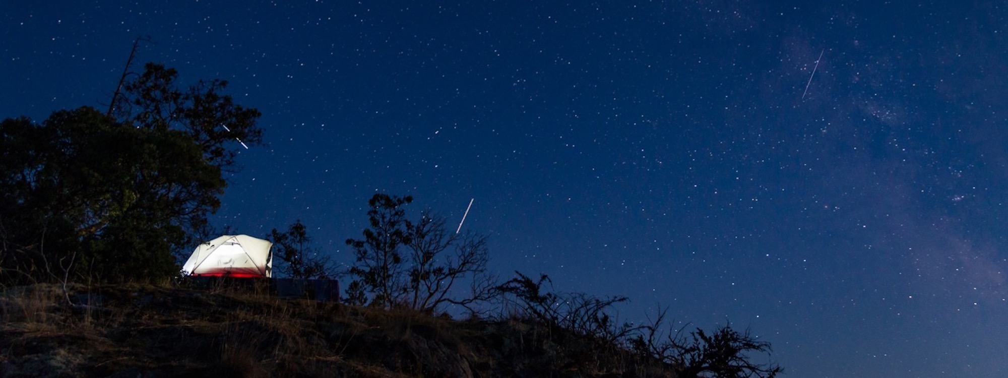 the night sky with stars above a tent and trees