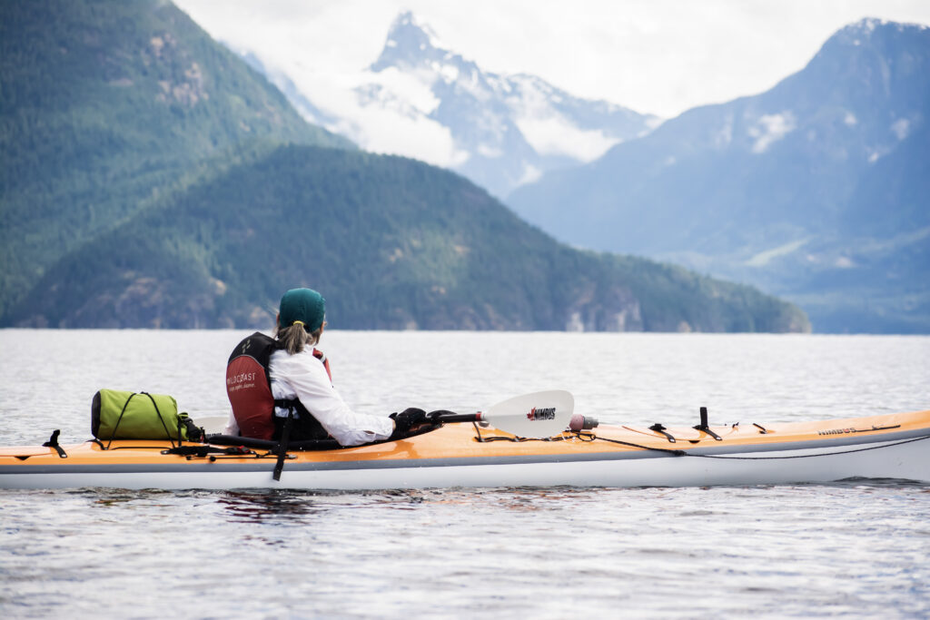 Sea kayaker paddling beneath snow-capped coastal mountains in Desolation Sound