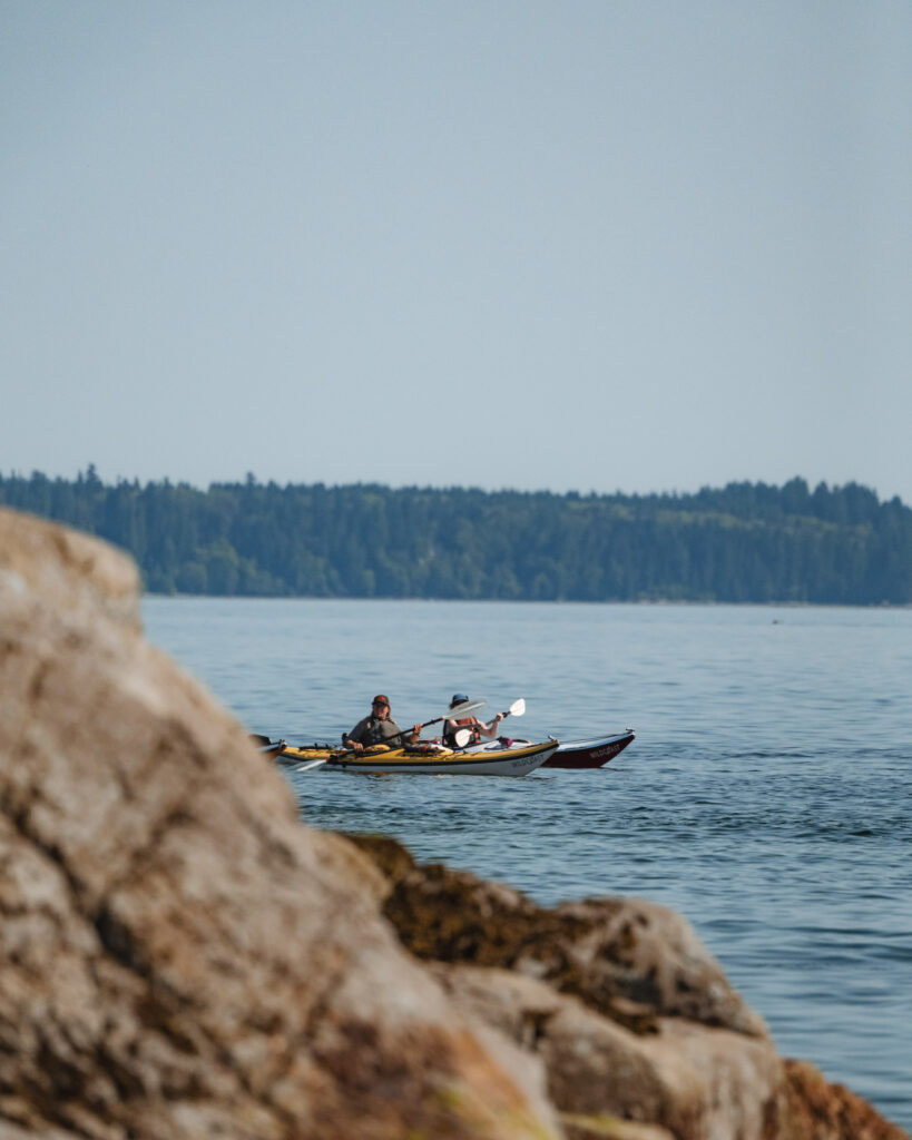 Two sea kayakers paddling past a rocky shoreline in the Discovery Islands