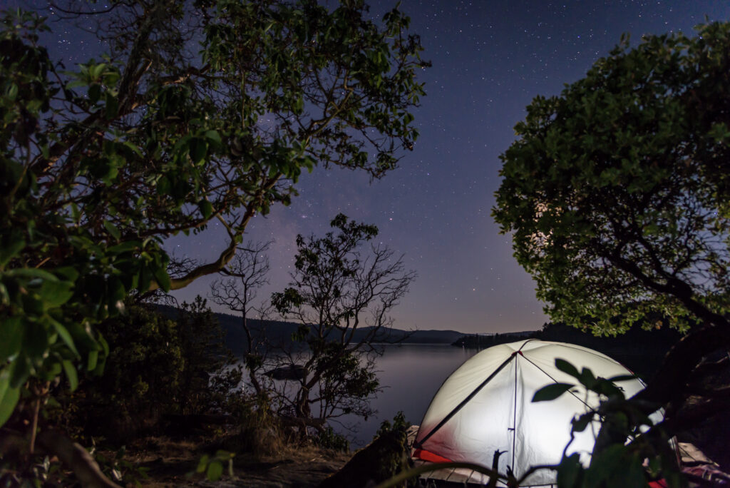 Tent glowing beneath the Milky Way at a waterfront campsite in Desolation Sound