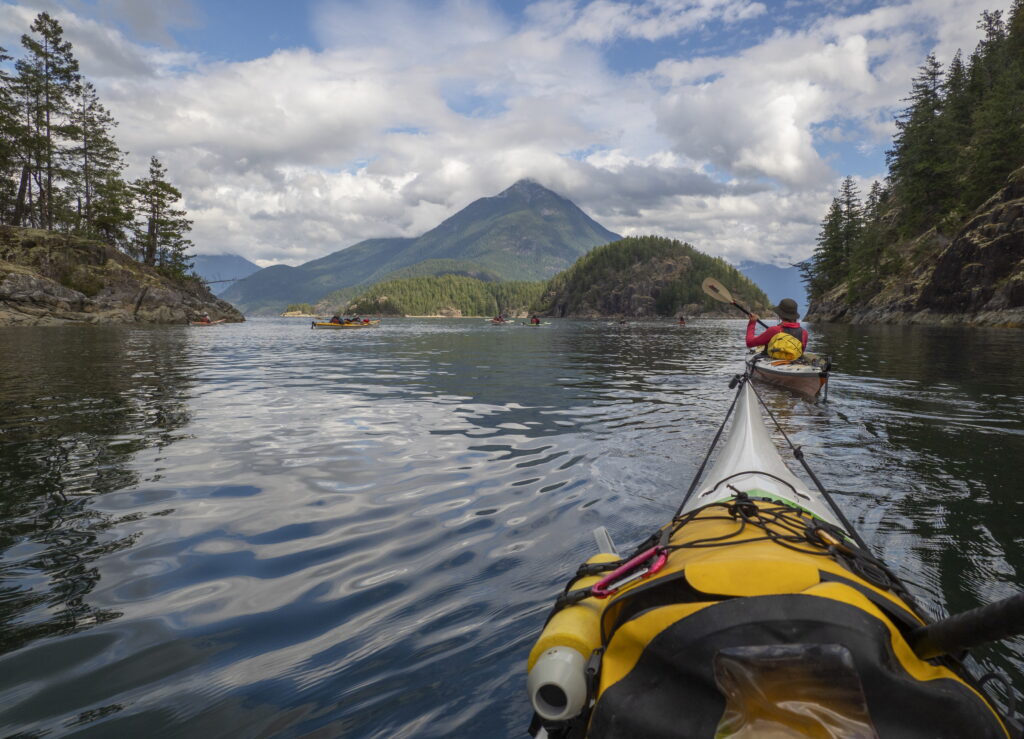 View from a sea kayak paddling calm water toward a mountain in Desolation Sound