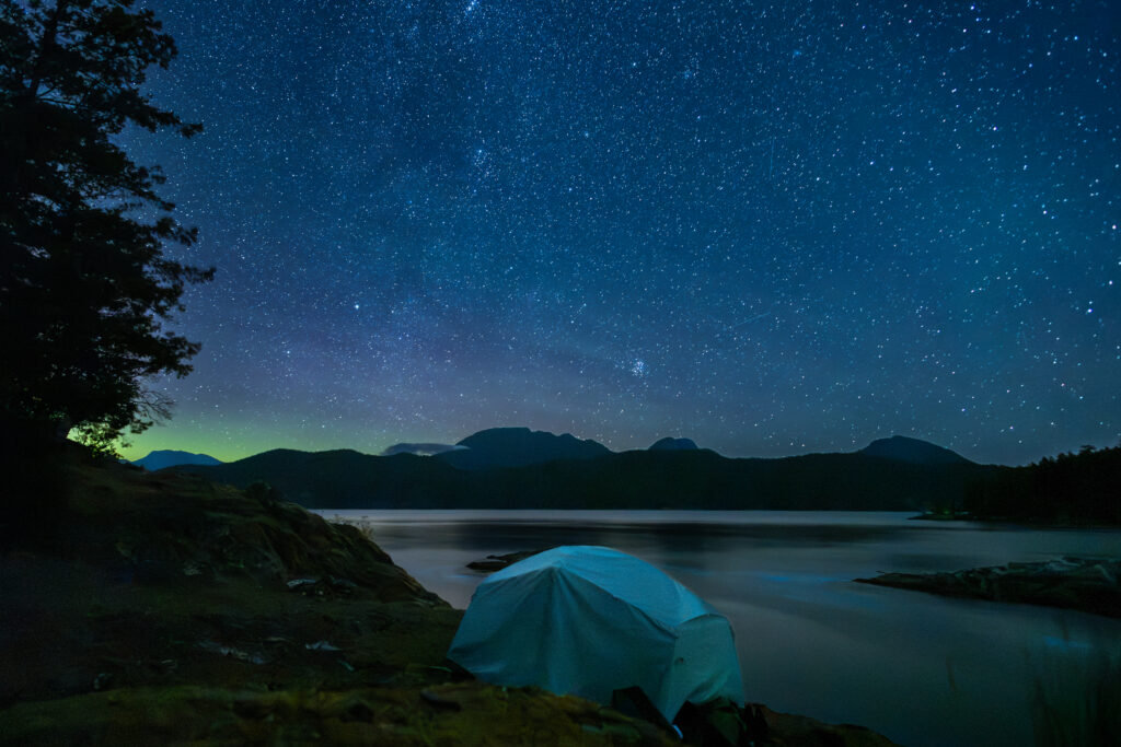Tent glowing under a starry sky beside the water in the Discovery Islands