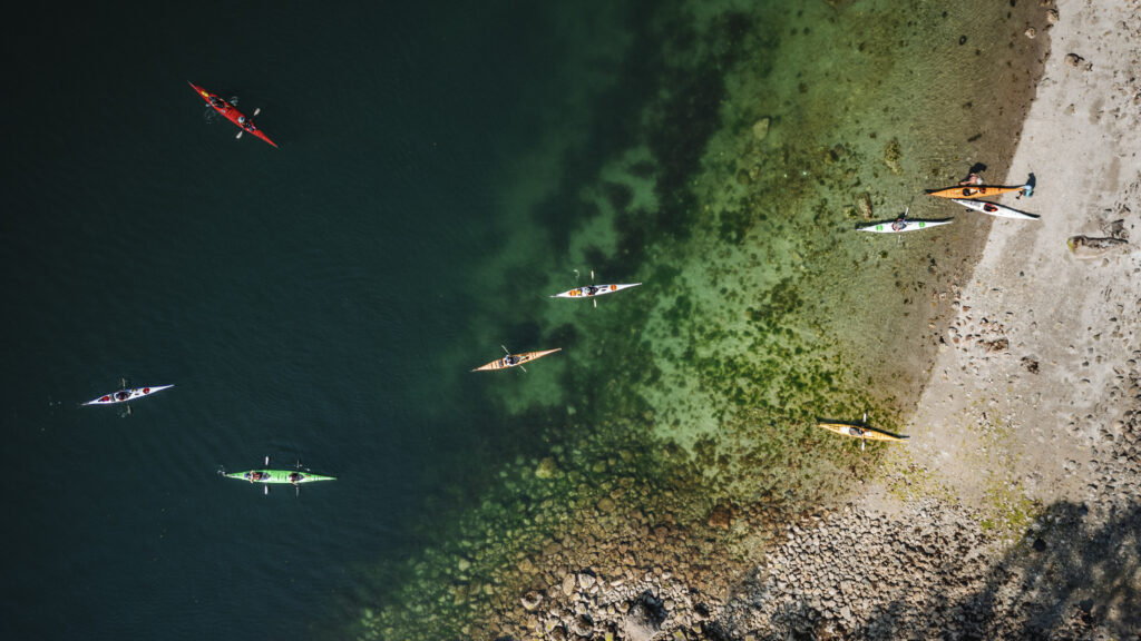 Aerial view of a group of sea kayaks over clear green water along a beach