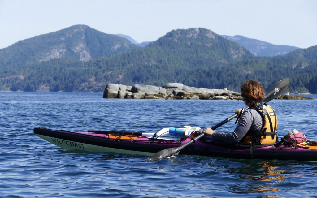 Sea kayaker paddling toward rocky islets and coastal mountains
