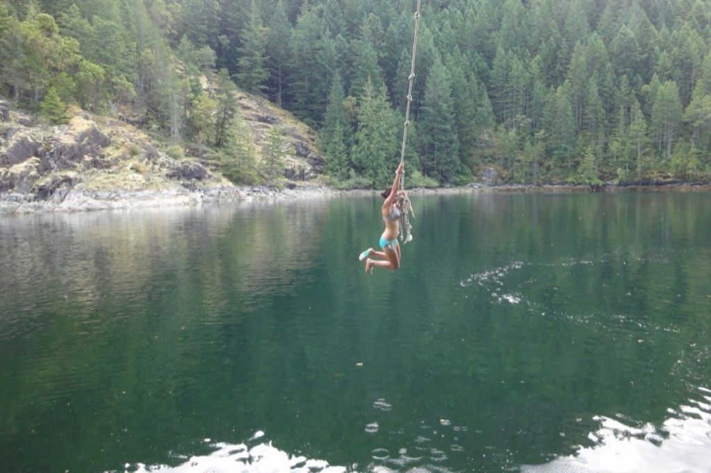 a woman hanging from a rope above the water