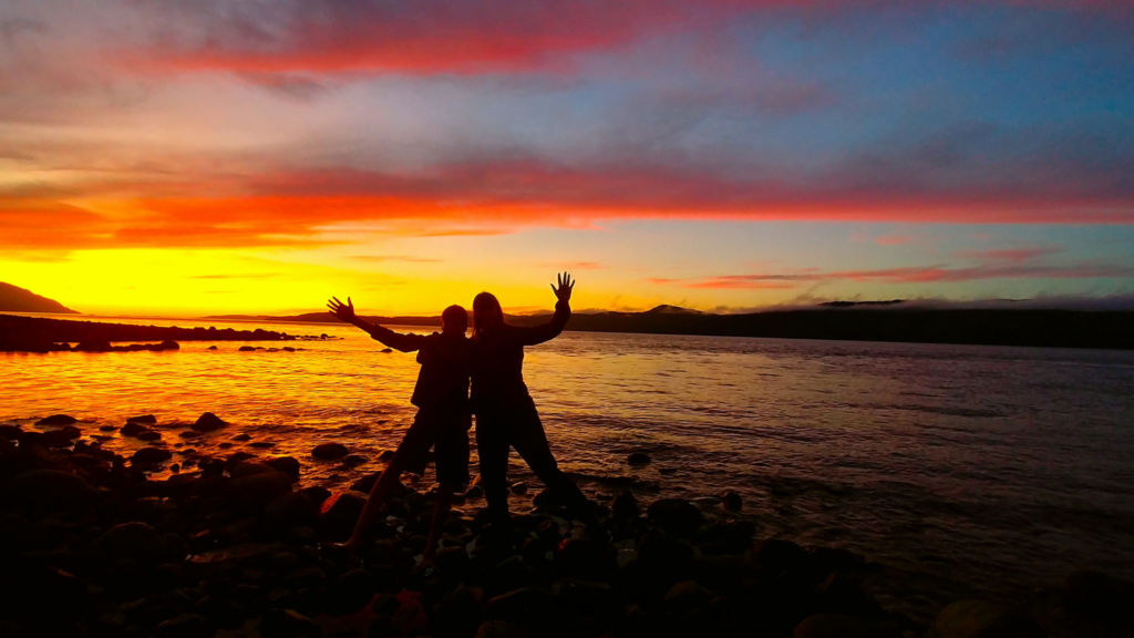 two people are standing on the shore with their arms in the air